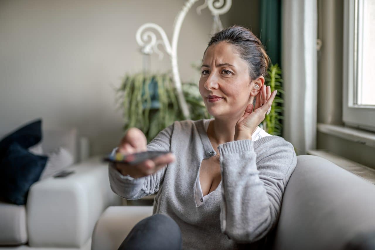 Adult woman with hearing aid watching television and adjusting her device.