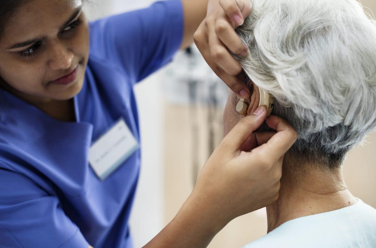 Senior woman being fitted for a hearing aid by a medical professional.