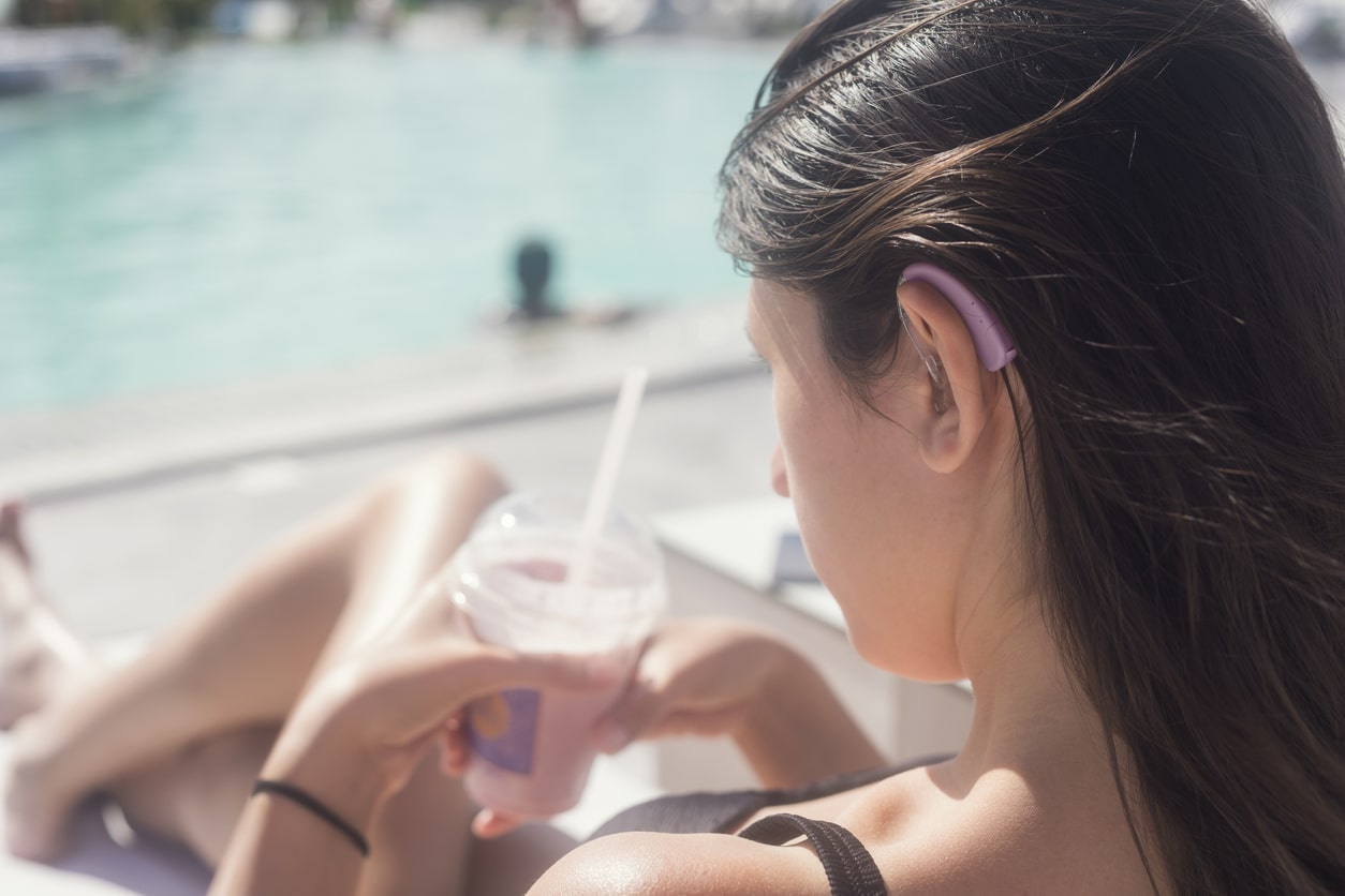 Woman sitting by the pool with a hearing aid in her ear.