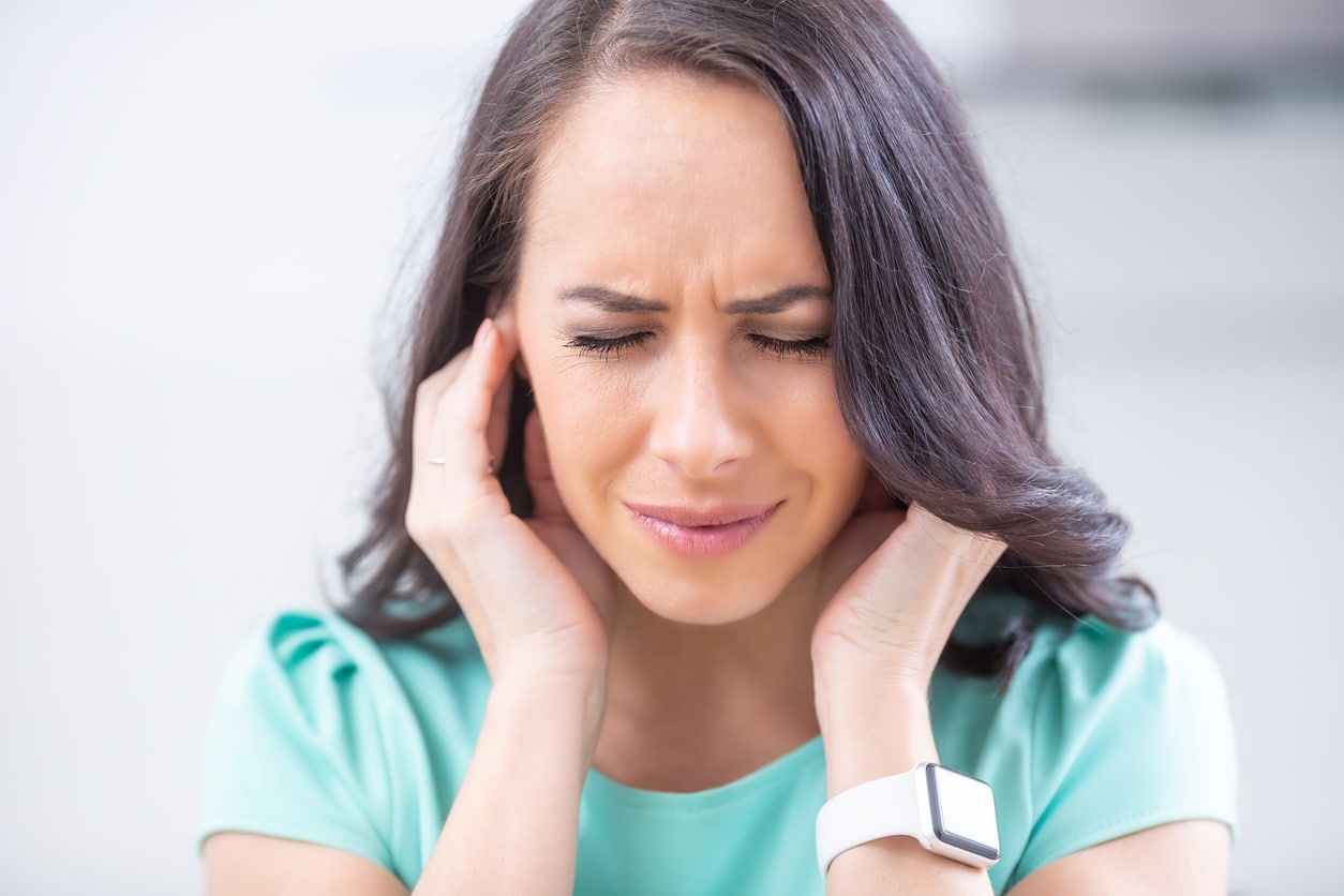 Young woman holding her ears because of tinnitus.