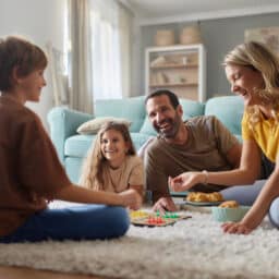 Happy parents and their kids playing a game on carpet at home.