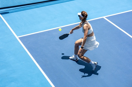 High-angle view of a female pickleball player hitting a backhand shot outdoors.